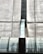 The image depicts an industrial structure featuring a large metal duct or vent running vertically against a concrete wall. The surface of the duct has a worn, metallic appearance with visible weathering and age. The concrete wall is segmented by horizontal and vertical lines, giving a geometric and symmetrical look.
