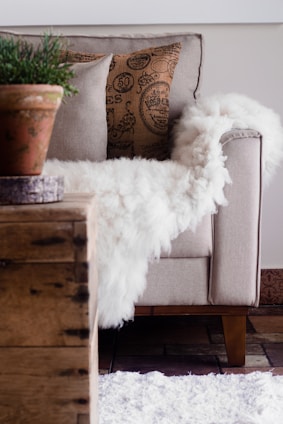 A soft faux fur throw draped over a comfy armchair beside a knitted pillow and a tassel garland hanging nearby.