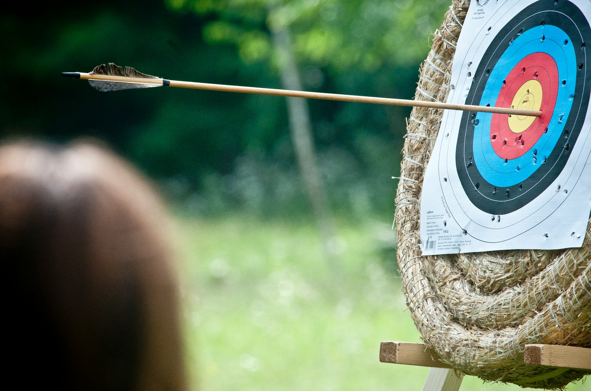 An archery target with many scattered punctures and an arrow that has almost hit the innermost ring.