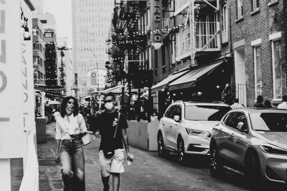 a man and woman walking down a street with cars parked on the side