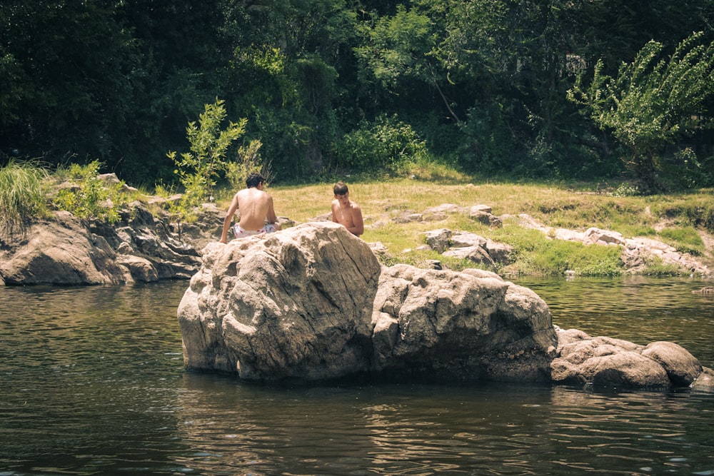 two men sitting on a rock in a river