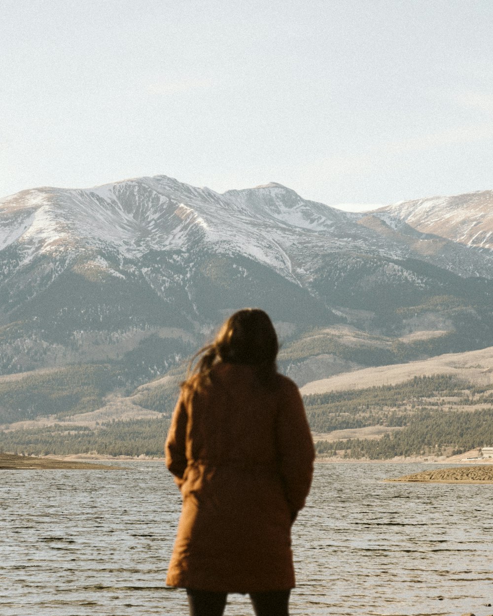 a person standing in front of a lake with a mountain in the background