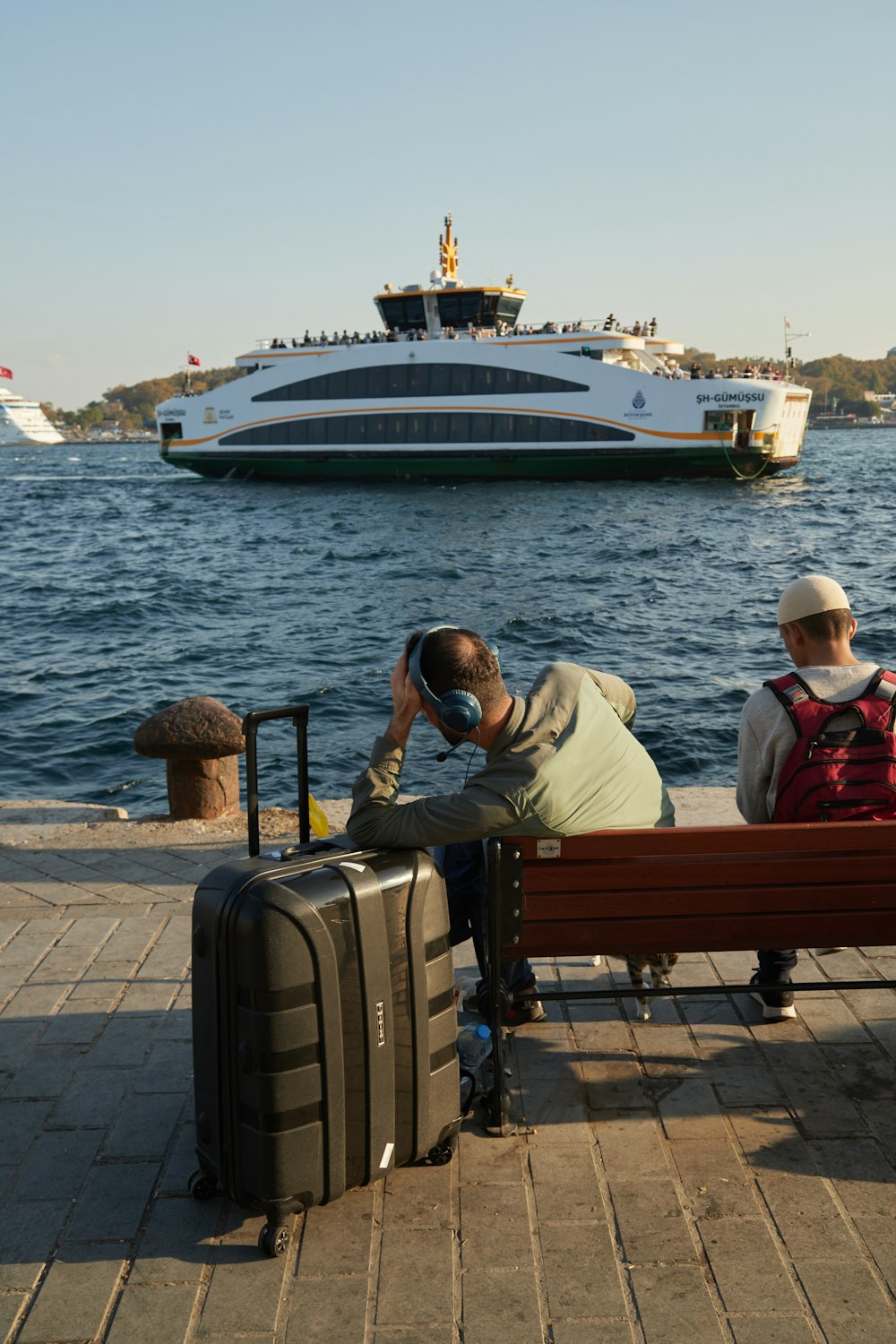 a person sitting on a bench with a suitcase and a large ship in the background