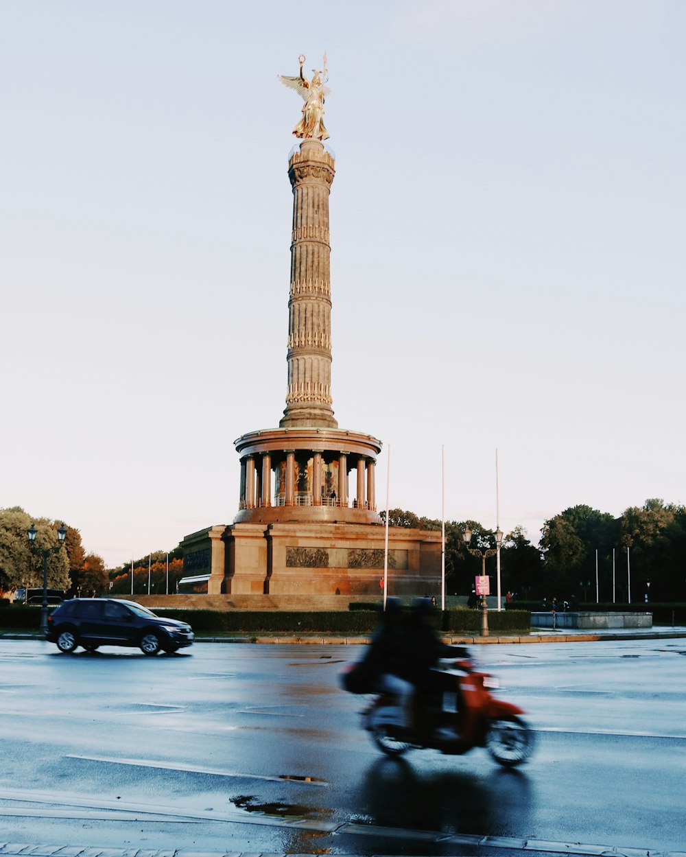 a person riding a motorcycle in front of a tall tower with Berlin Victory Column in the background