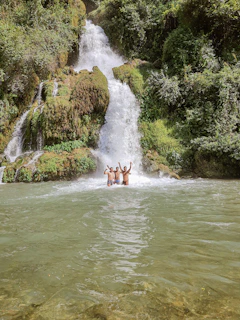 Smiling kids splashing in a natural Jamaican waterfall pool surrounded by greenery.