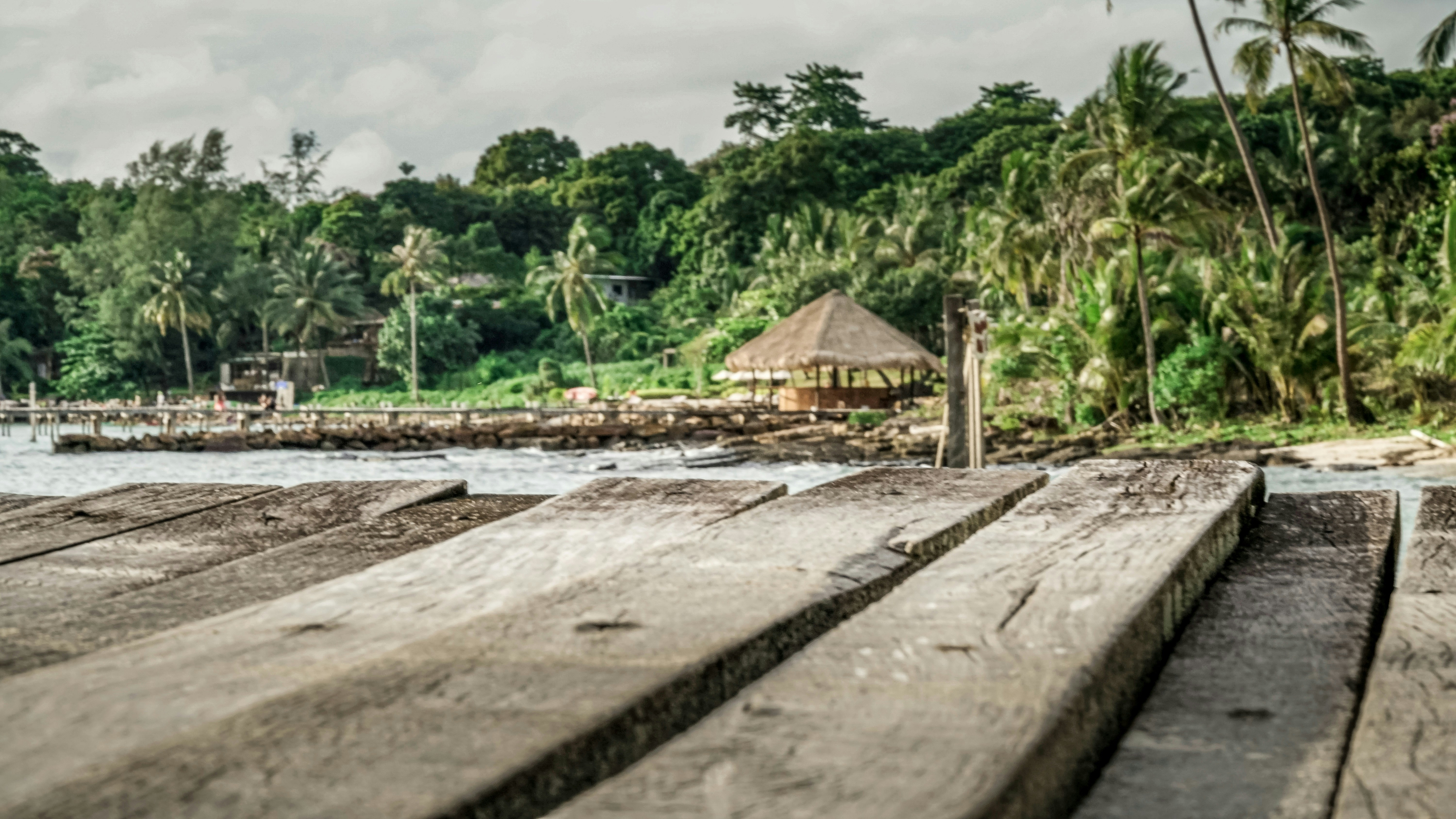 a stone wall with a building and trees in the background, Wooden Pier on the island of Koh Kood, Thailand
