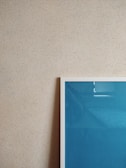 A textured beige wall is adorned with a framed artwork. The frame has a white border and contains a blue-colored piece. The photo captures a minimalist and modern aesthetic.