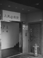 A black and white photograph of a doorway leading into a stairwell. The entrance is located between a spa sign and a heavy-looking door marked with the number 489. Adjacent to the door, a fire hydrant is noticeable on the sidewalk.
