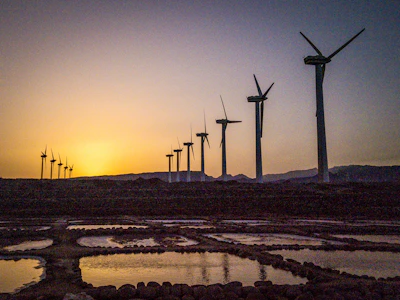 Solar panels and wind turbines set against a vibrant sunrise.