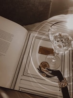 A sophisticated evening setting: a glass of spirit on a polished surface, a leather-bound book, and dim, moody lighting.