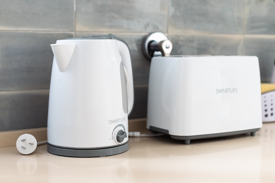 A white electric kettle and toaster are placed on a beige countertop against a tiled backsplash. Both appliances are labeled 'SMARTLIFE' and have a sleek, modern design. The kettle is plugged in, with the power cord visible.