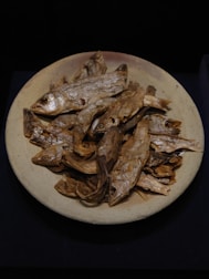 A plate filled with several dried fish, arranged in a somewhat haphazard manner. The fish have a distinctly brown and desiccated appearance, indicating they have been preserved.