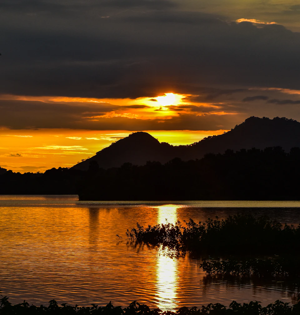 Serene sunset over a lake with mountains in the background casting warm glow