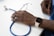 A person's hand rests on a table next to a stethoscope. The person is wearing a smartwatch on their wrist and is dressed in scrubs, suggesting a medical professional setting.