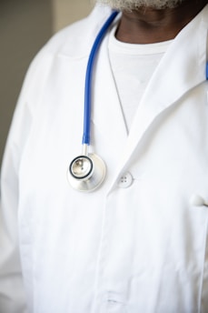 A person wearing a white lab coat with a blue stethoscope draped around their neck. The focus is on the upper body, highlighting the medical attire typically associated with healthcare professionals.