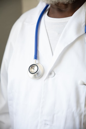 A person wearing a white lab coat with a blue stethoscope draped around their neck. The focus is on the upper body, highlighting the medical attire typically associated with healthcare professionals.