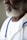 A close-up of a person with a white beard wearing a white coat and a stethoscope around their neck. The focus is on the person's lower face and upper chest.