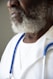 A close-up of a person with a white beard wearing a white coat and a stethoscope around their neck. The focus is on the person's lower face and upper chest.