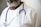A person wearing a white lab coat and a blue stethoscope around their neck. The individual has a graying beard and is wearing a white shirt underneath the lab coat.