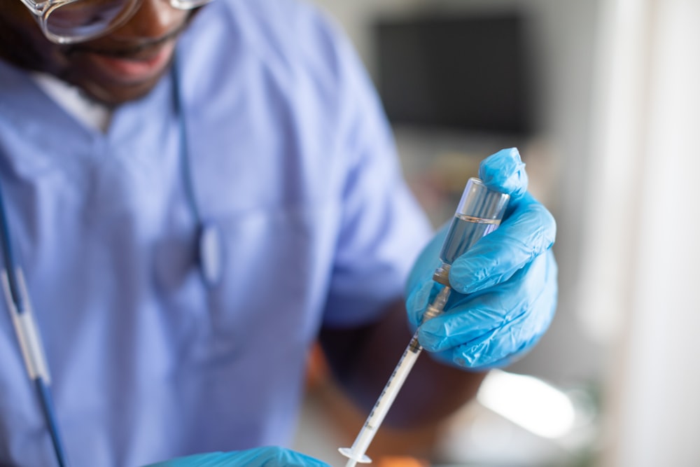 a person wearing a lab coat and gloves holding a syringe