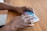 Hands are handling a weekly medication organizer placed on a wooden table. The organizer has compartments labeled with days of the week, and the colors of the compartments vary from purple to blue.