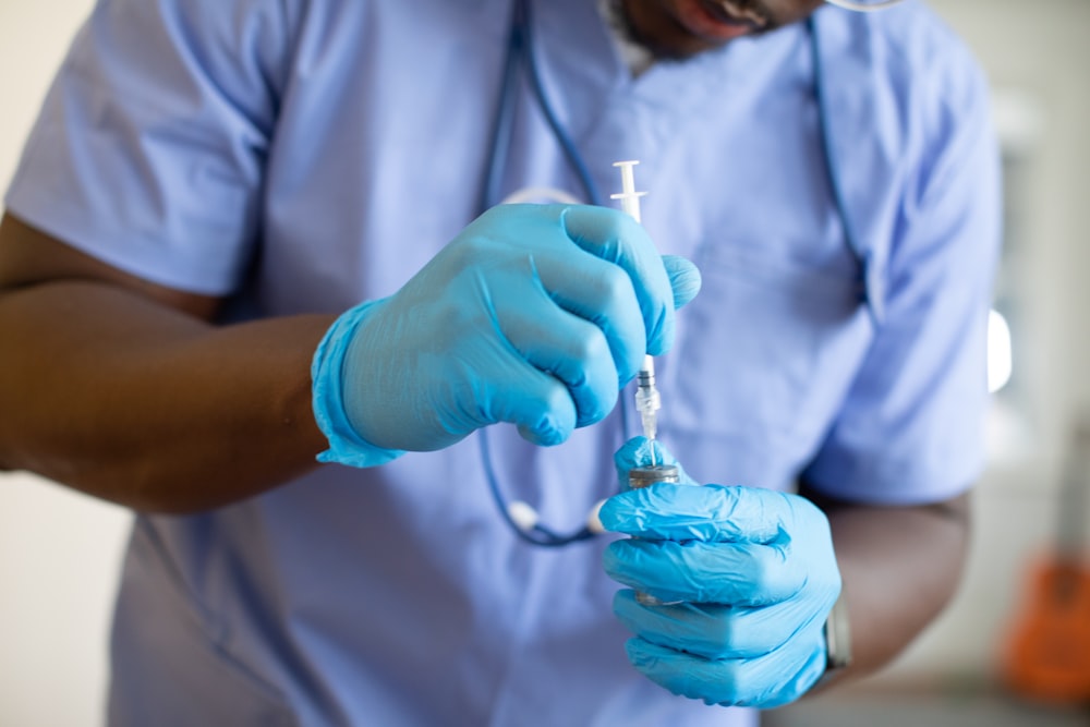 a person wearing gloves and a blue lab coat holding a syringe