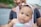 A smiling parent holding a baby in a cute outfit at a sunny park.