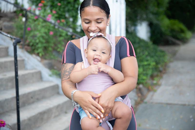 A smiling mother gently holding her baby while using a smartphone app.