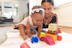 A smiling toddler playing with colorful blocks under the watchful eye of a warm, caring babysitter.