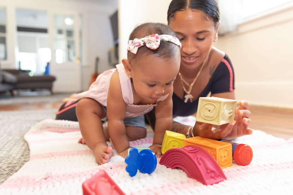 a woman and a baby playing with toys on a blanket