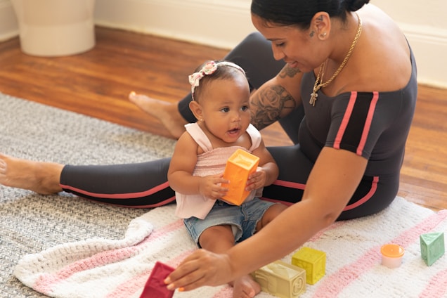 A cozy scene of a parent and toddler playing a colorful developmental game on a soft blue and sand-colored rug.