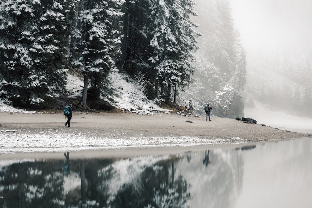 a couple people walking on a snowy path by a lake