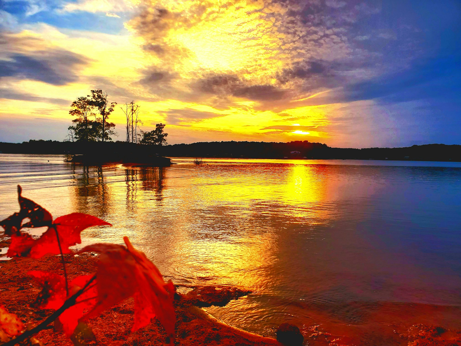 A vibrant sunset reflecting off the calm lake surface, with an infallible kayak resting gently near the shore surrounded by autumn leaves.
