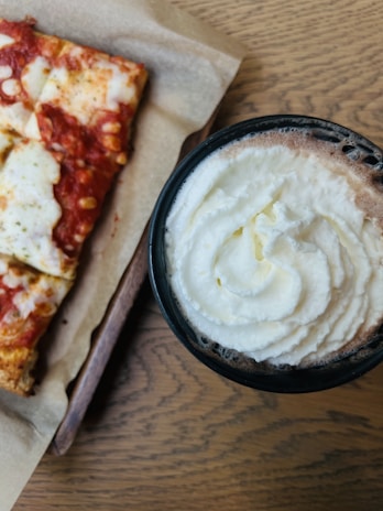 Close-up of a steaming cup of coffee beside a perfectly baked woodfire pizza slice.