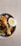 A bowl of biryani rice with pieces of chicken and a halved boiled egg. The dish is garnished with fresh green herbs and served in a white speckled bowl placed on a wooden surface.