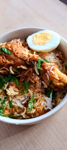 Close-up of steaming chicken biryani with vibrant spices and herbs.