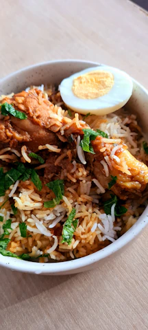 A close-up shot of a steaming clay pot biryani with vibrant spices and fresh herbs on top.