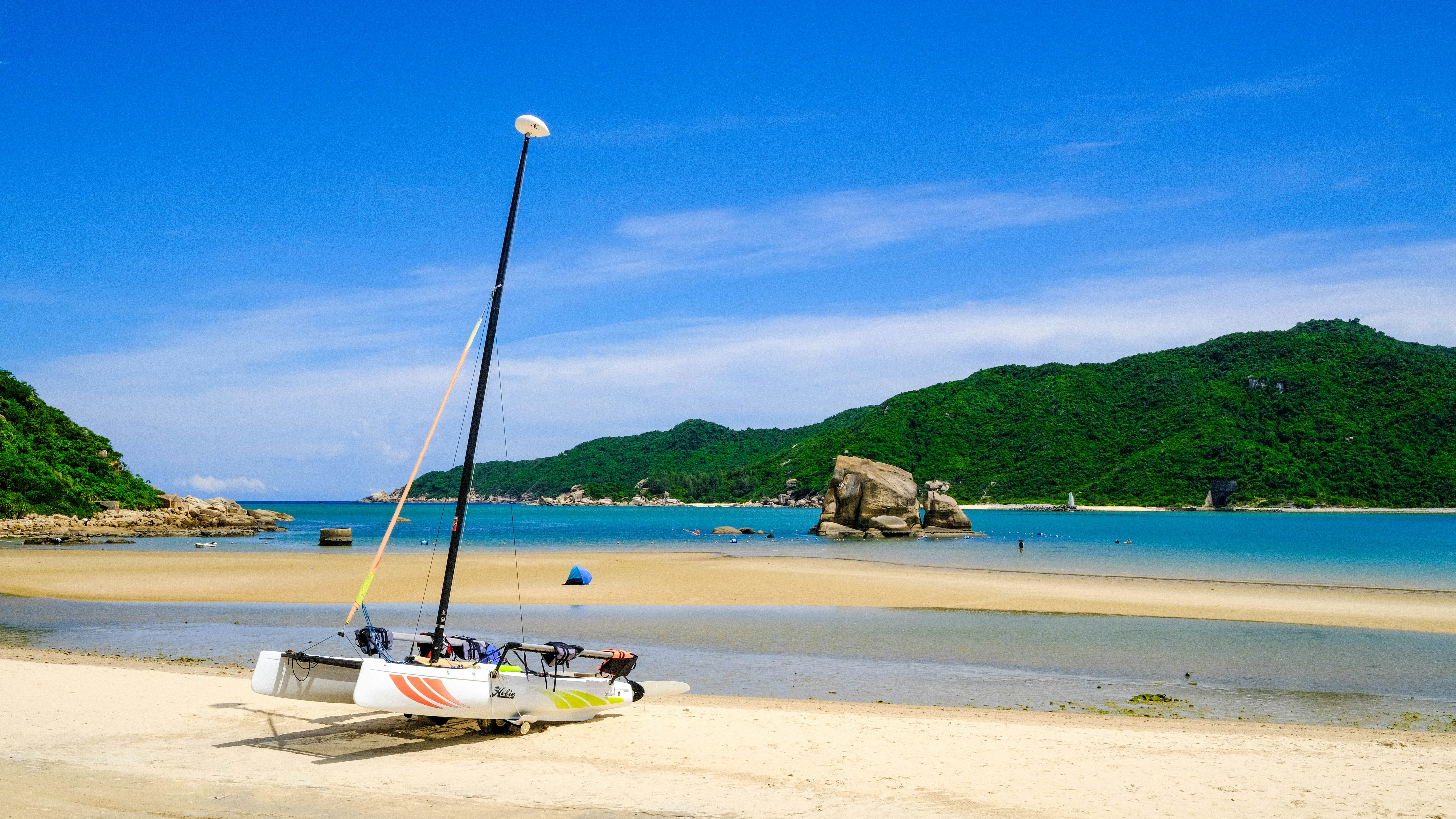 White sailboat anchored in turquoise bay with green hills behind