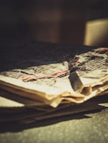 A close-up view of a crumpled newspaper featuring printed text. The paper is aged or weathered, with a yellowish tint. Shadows and light create a dramatic effect across the surface.