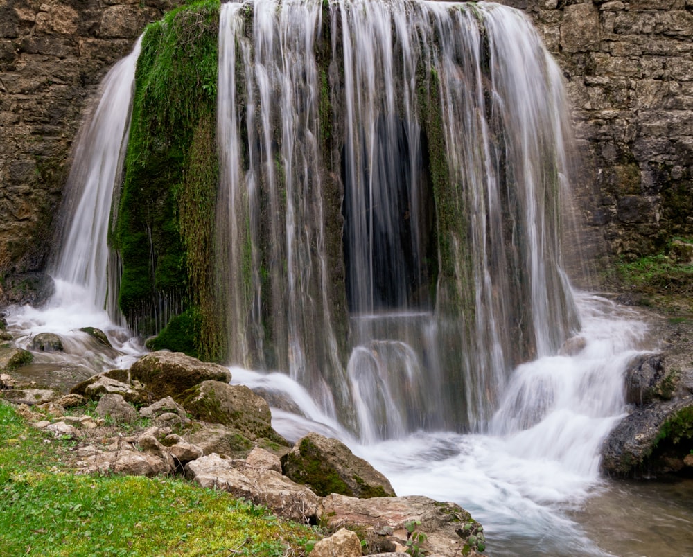 a waterfall with rocks and grass