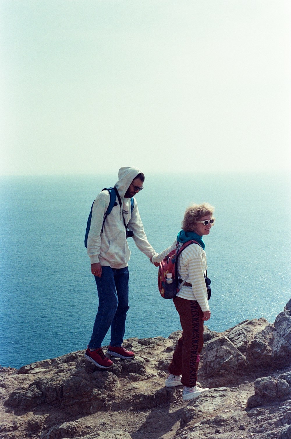 a man and woman standing on a rocky cliff overlooking the ocean
