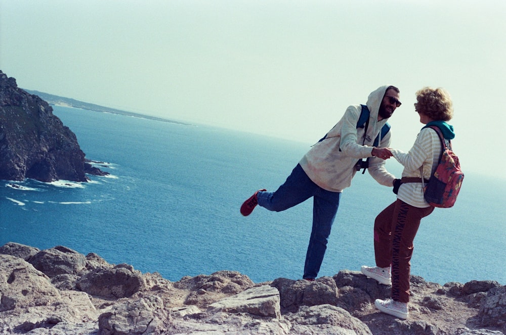 a man and woman standing on a rocky cliff overlooking the ocean