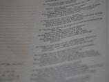 A page from a book with printed text, featuring numbered verses that appear poetic. The text is aligned along the center, and the image is slightly out of focus, particularly towards the bottom. The paper has a faint texture, with visible lines to the left side.