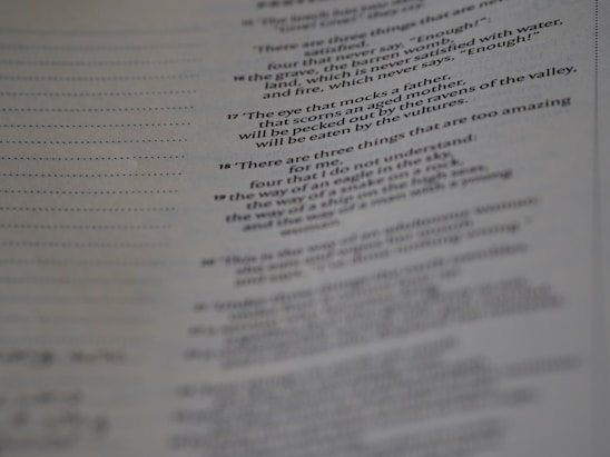 A page from a book with printed text, featuring numbered verses that appear poetic. The text is aligned along the center, and the image is slightly out of focus, particularly towards the bottom. The paper has a faint texture, with visible lines to the left side.