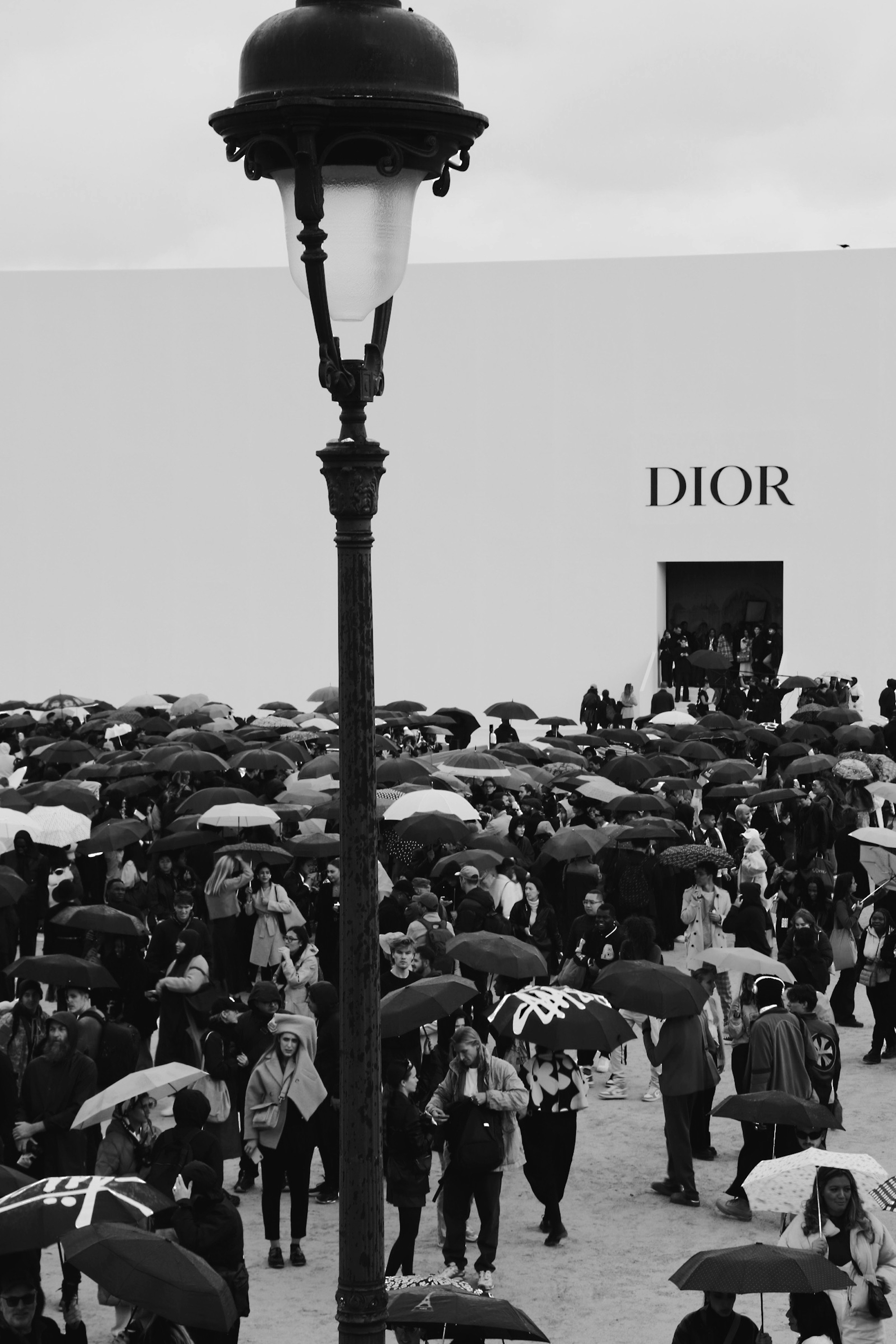 Fashion week attendees in avant-garde street style outfits outside Paris venue, overcast moody sky, urban setting