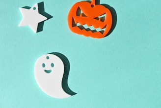 A light blue background hosts three Halloween-themed decorations: a white star, an orange jack-o'-lantern with a mischievous grin, and a happy white ghost.