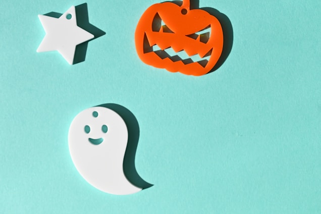 A light blue background hosts three Halloween-themed decorations: a white star, an orange jack-o'-lantern with a mischievous grin, and a happy white ghost.