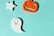 A light blue background hosts three Halloween-themed decorations: a white star, an orange jack-o'-lantern with a mischievous grin, and a happy white ghost.