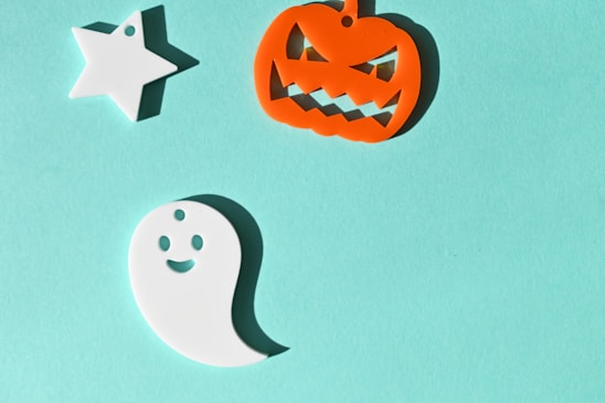 A light blue background hosts three Halloween-themed decorations: a white star, an orange jack-o'-lantern with a mischievous grin, and a happy white ghost.