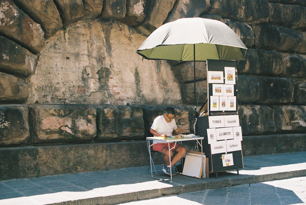 uma pessoa sentada em uma mesa sob um guarda-chuva